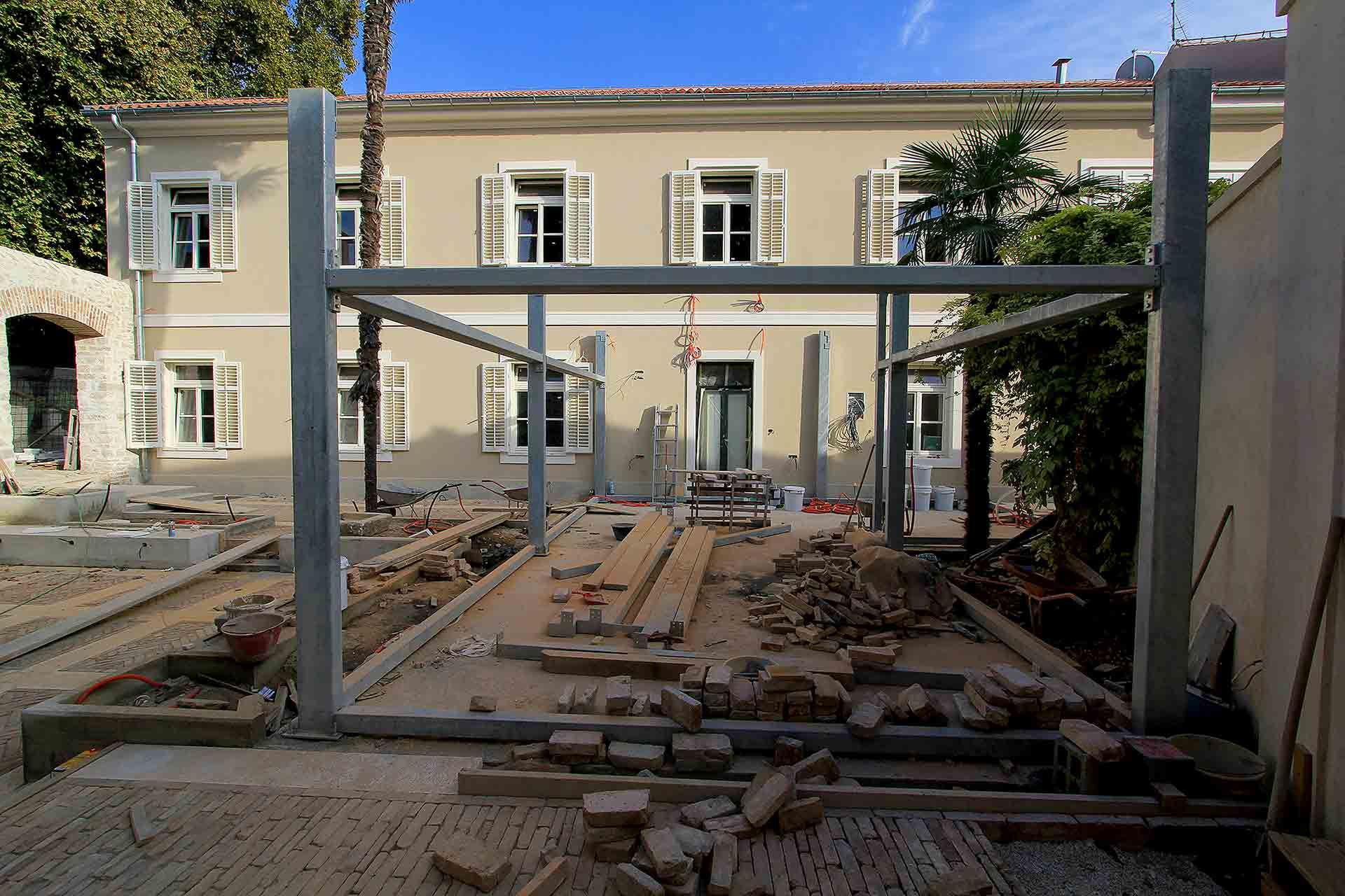 A view of the freshly painted facade of the future Almayer Hotel, alongside the construction of a glazed steel orangery and the landscaping of the secret garden