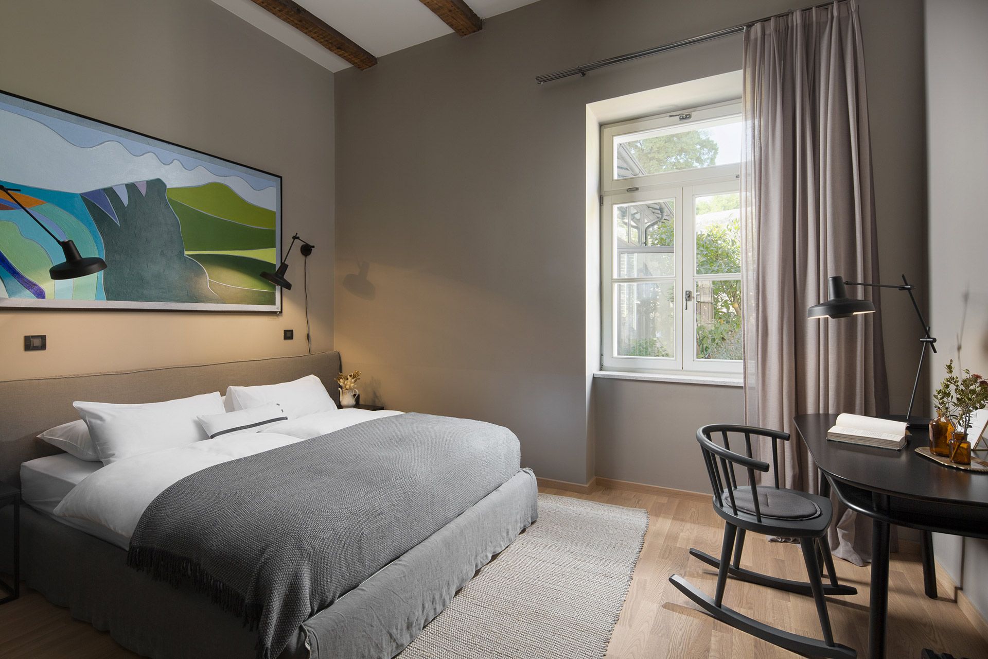 A relaxing interior design of the standard double room Levante in Almayer Art & Heritage Hotel and its comfortable king size bed, desk, painting, and bright window with a garden view